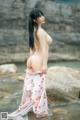 A woman in a white bikini standing on a rock by the water.