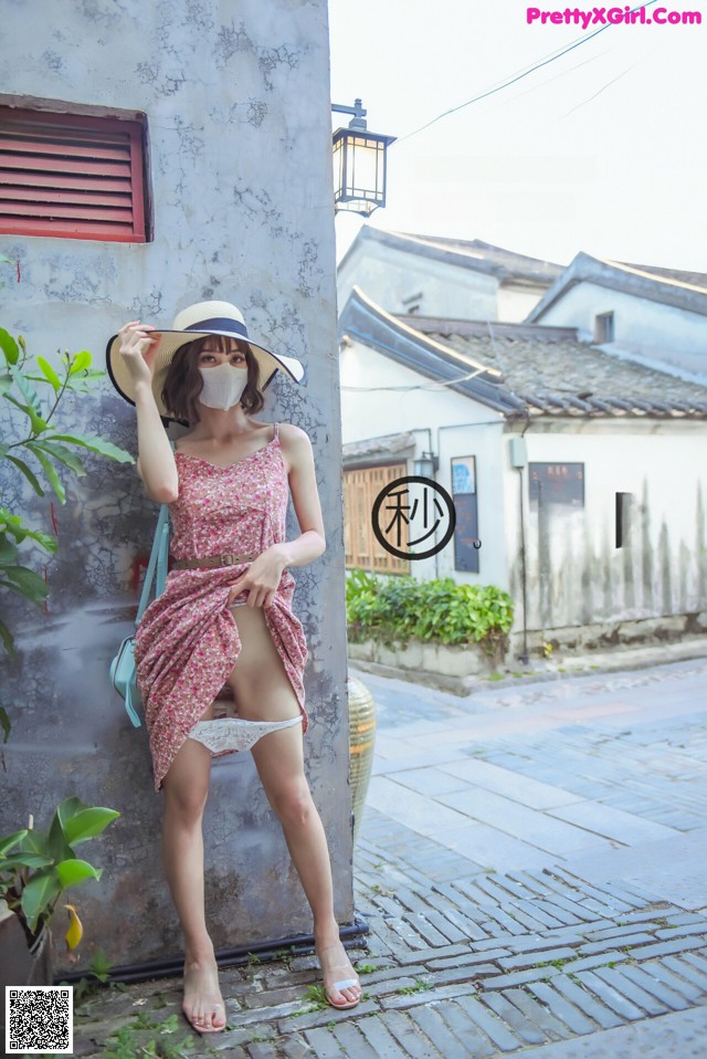 A woman wearing a hat and a face mask leaning against a wall.