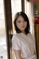 A woman in a white shirt leaning against a window.