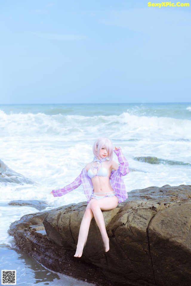 A woman sitting on a rock by the ocean.